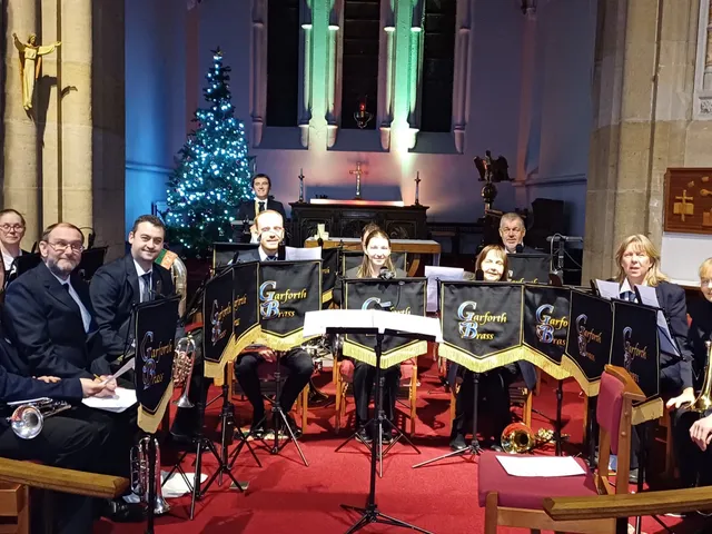 Garforth Brass seated in a church beside a Christmas tree, ready to perform.